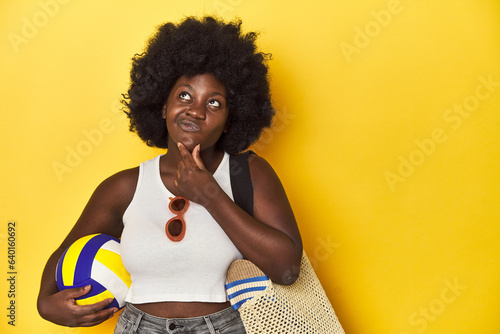 Beach-ready woman with volleyball, ready for sport looking sideways with doubtful and skeptical expression.