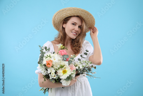 Beautiful woman in straw hat with bouquet of flowers on light blue background