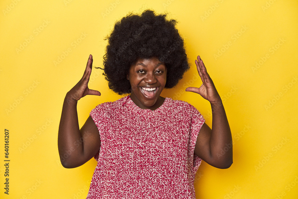 African-American woman with afro, studio yellow background joyful laughing a lot. Happiness concept. African-American woman with afro, studio yellow background joyful laughing a lot. Happiness concept.