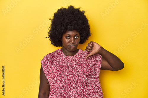 African-American woman with afro, studio yellow background showing a dislike gesture, thumbs down. Disagreement concept. © Asier