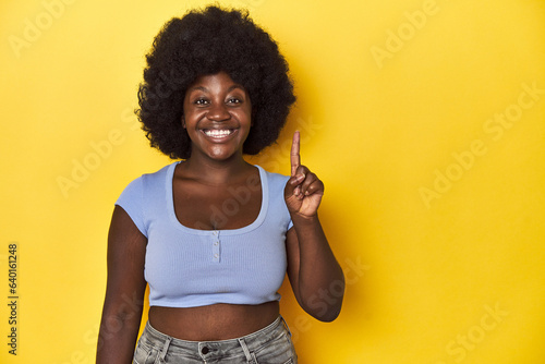 African-American woman with afro, studio yellow background showing number one with finger.