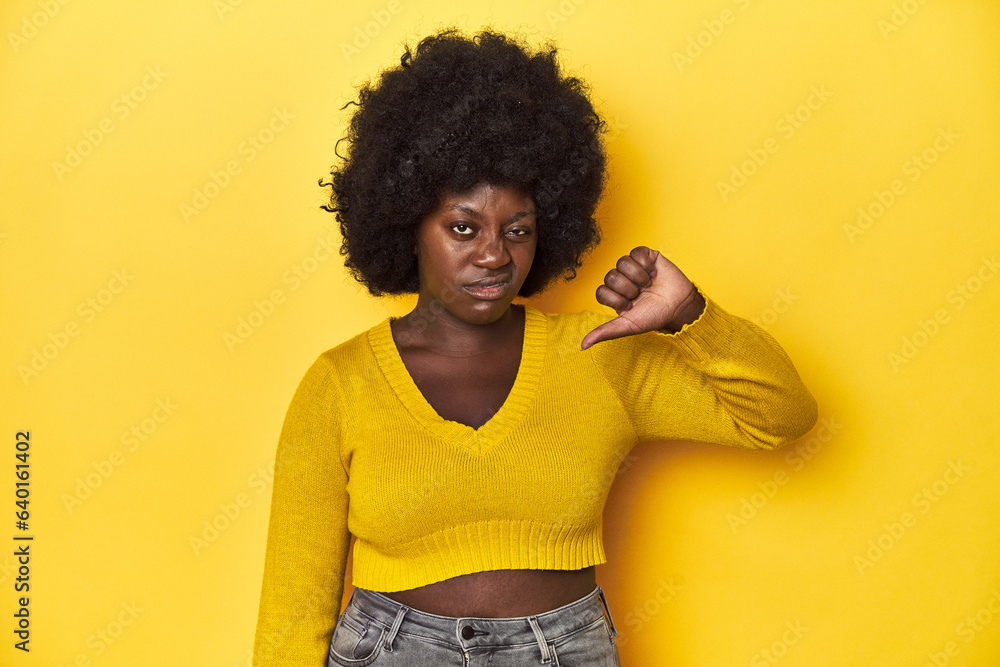 African-American woman with afro, studio yellow background showing thumb down, disappointment concept. African-American woman with afro, studio yellow background showing thumb down, disappointment concept.