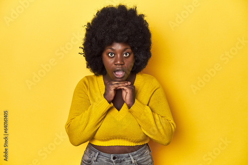 African-American woman with afro  studio yellow background praying for luck  amazed and opening mouth looking to front.