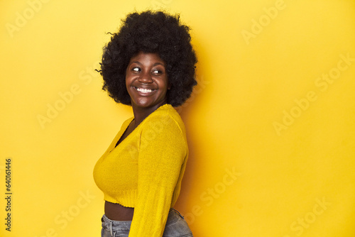 African-American woman with afro, studio yellow background looks aside smiling, cheerful and pleasant. © Asier