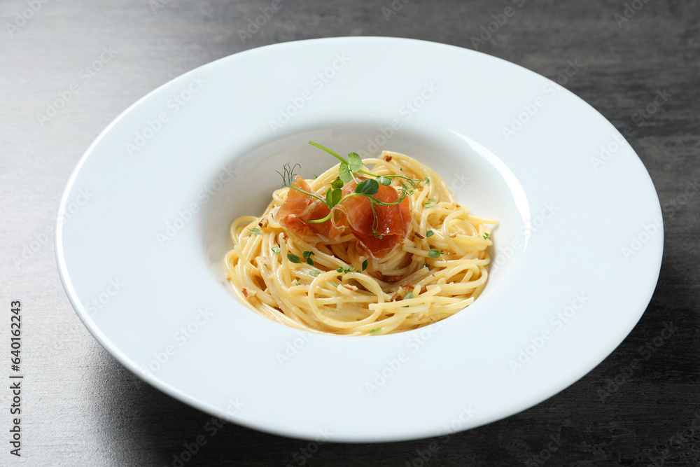Tasty spaghetti with prosciutto and microgreens on grey textured table, closeup. Exquisite presentation of pasta dish