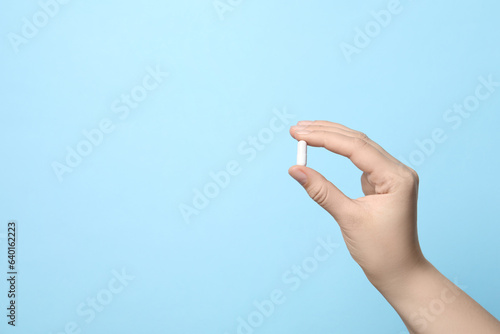 Woman holding pill on light blue background, closeup. Space for text