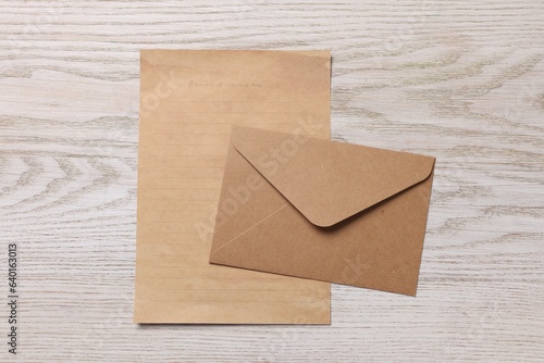 Envelope and sheet of parchment paper on white wooden table, flat lay