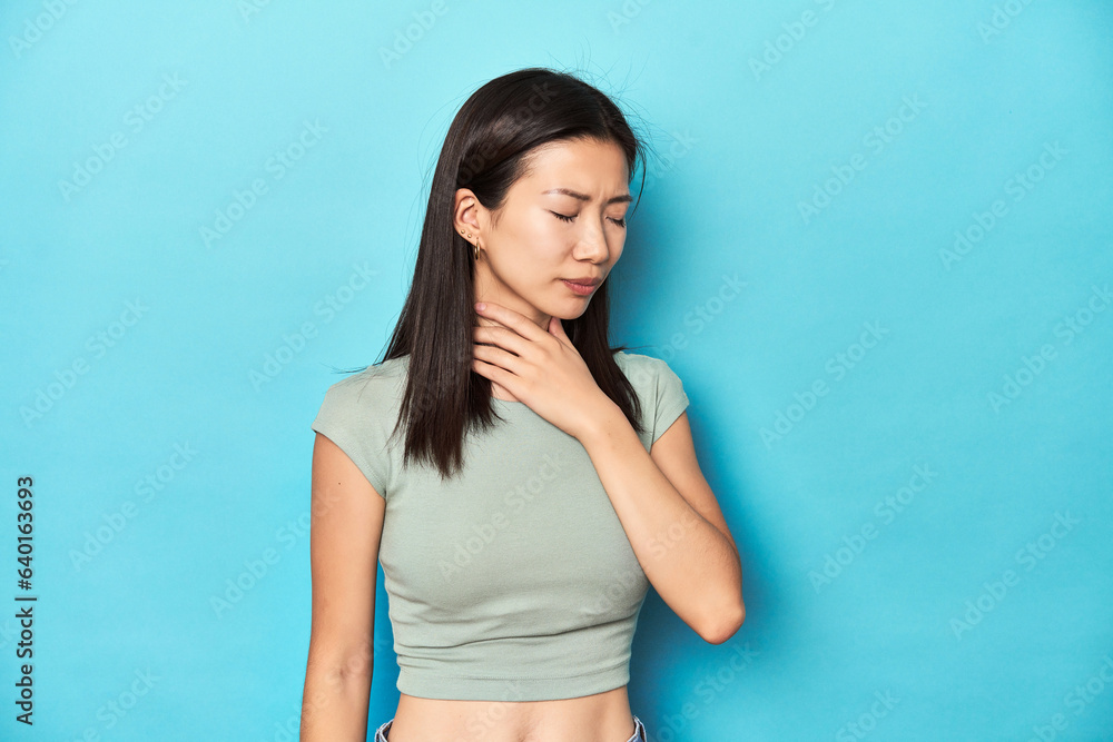 Asian woman in summer green top, studio backdrop, suffers pain in throat due a virus or infection. Asian woman in summer green top, studio backdrop, suffers pain in throat due a virus or infection.