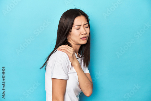Young Asian woman in white t-shirt, studio shot, having a shoulder pain.