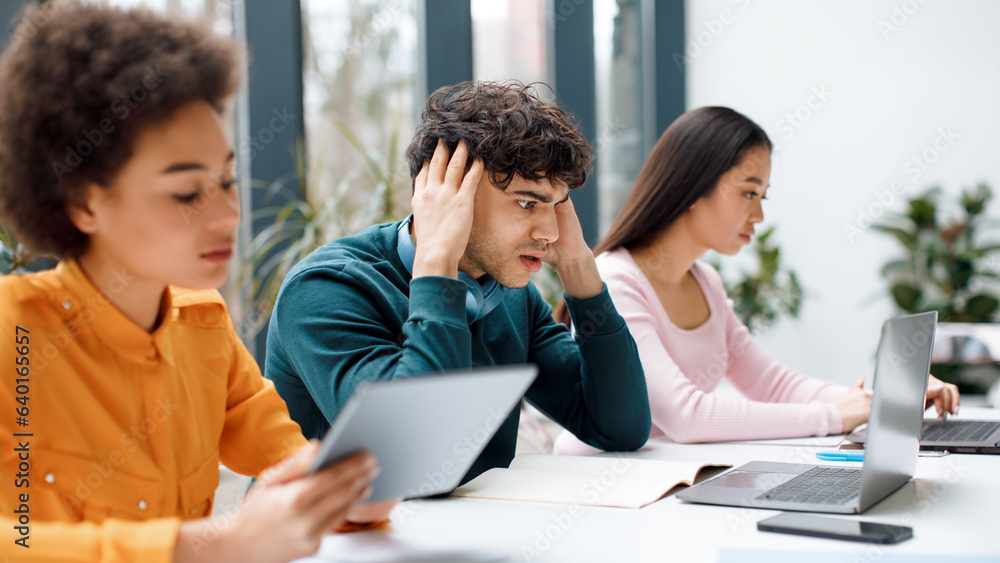 Worried sad student guy looking at laptop, getting final test results, sitting with groupmates in audience Worried sad student guy looking at laptop, getting final test results, sitting with groupmates in audience
