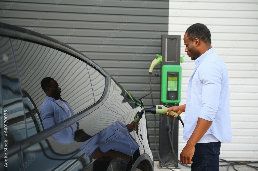 African American man charging his electric car. African American man charging his electric car.