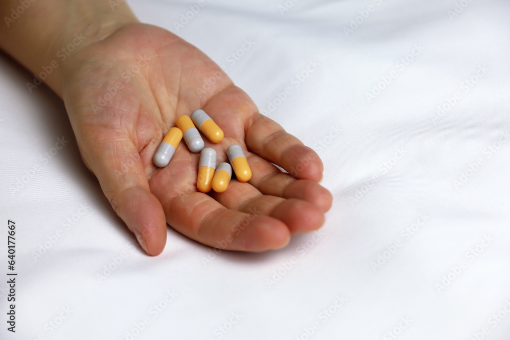 Pills in a palm of female hand on the bed. Concept of medication, vitamins or sleeping pill Pills in a palm of female hand on the bed. Concept of medication, vitamins or sleeping pill