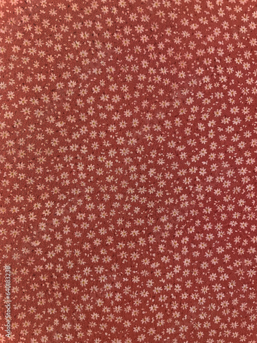 Fabric with seamless vintage ditsy floral pattern, closeup as a texture. Old fashioned, retro style cotton or linen textile with a print of scattered small yellowish flowers on rust red background