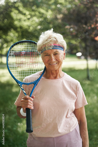 Portrait of senior woman standing in the park and holding tennis racket © gpointstudio