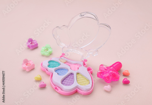 Decorative cosmetics for kids. Eye shadow palette and accessories on pink background