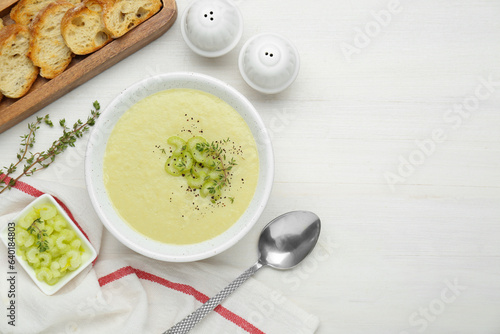 Bowl of delicious celery soup served on white wooden table, flat lay. Space for text