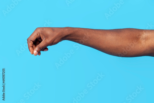african american male hand pours spices and salts on blue isolated background, the hand holds pinch