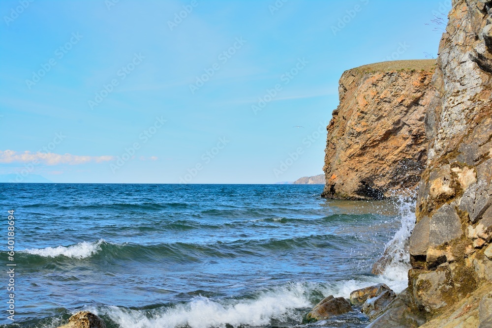 Scenic lake coast landscape rock waves. Blue sky and clear water.