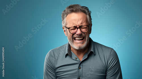 Depressed man in casual clothes crying on blue background