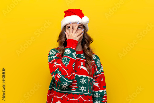 facepalm gesture. puzzled girl in christmas sweater and santa claus hat covers her face with her hand