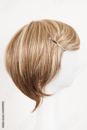 Natural looking blonde fair wig on white mannequin head. Short hair cut on the plastic wig holder isolated on white background, side view.