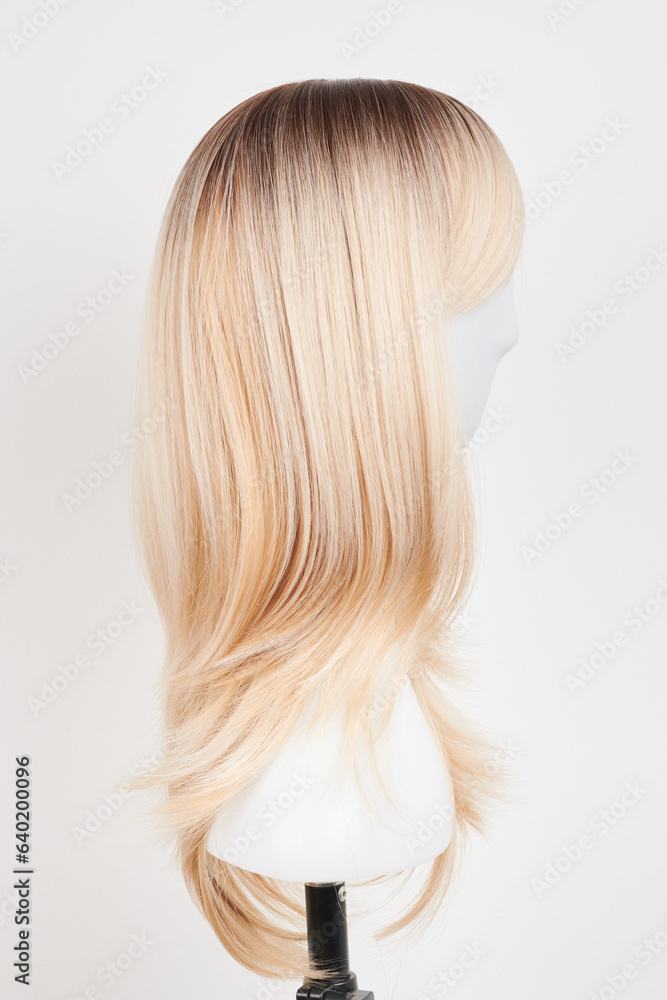 Natural looking blonde wig on white mannequin head. Long hair on the plastic wig holder isolated on white background, side view. Natural looking blonde wig on white mannequin head. Long hair on the plastic wig holder isolated on white background, side view.