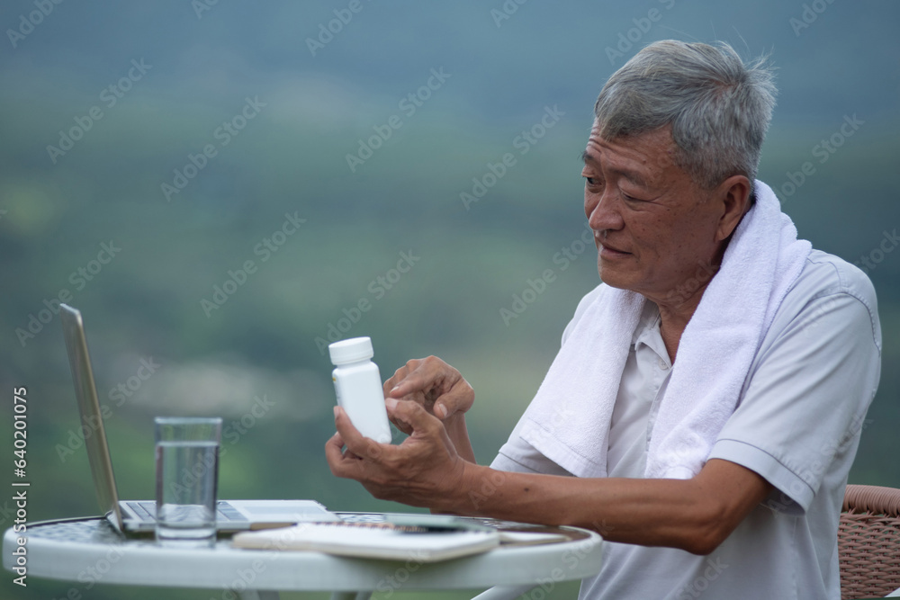 Asian old man is feeling unwell, like having a fever after exercising, sitting and holding medicine bottle reading label text about medical information, concept of healthy living in the elderly Asian old man is feeling unwell, like having a fever after exercising, sitting and holding medicine bottle reading label text about medical information, concept of healthy living in the elderly