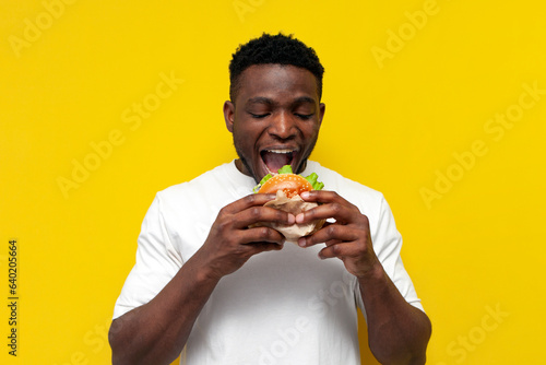 Принти на полотні african american man in white t-shirt bites big burger on yellow isolated backgr