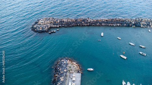 Barca ormeggiata nel porto vista dall'alto, fotografia con drone mostra la massicciata della marina, acqua del mare limpido ed una barca all'ormeggio photo