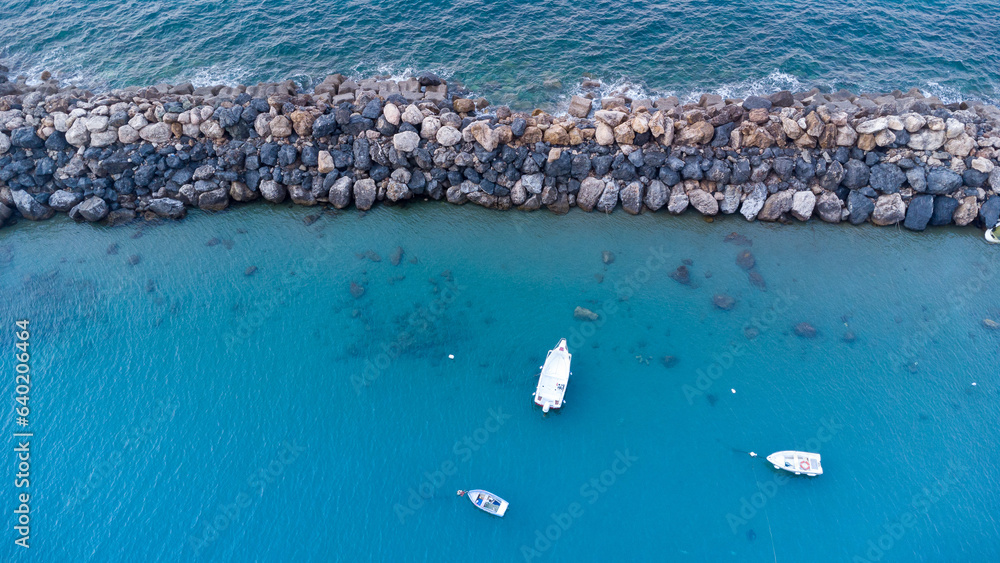 Barca ormeggiata nel porto vista dall'alto, fotografia con drone mostra la massicciata della marina, acqua del mare limpido ed una barca all'ormeggio - obrazy, fototapety, plakaty 