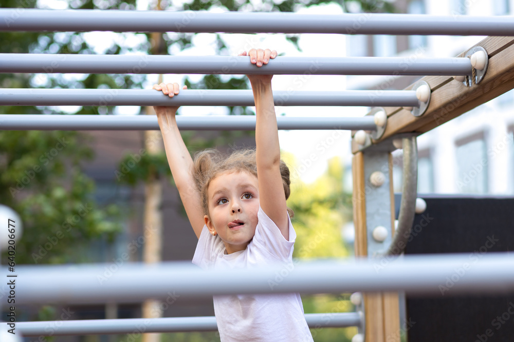 child sport. little active girl on playground in park, hanging on horizontal bar, rope ladder, workout, doing sports exercise outdoors. happy childhood. Kid play on school kindergarten yard in summer child sport. little active girl on playground in park, hanging on horizontal bar, rope ladder, workout, doing sports exercise outdoors. happy childhood. Kid play on school kindergarten yard in summer