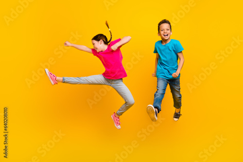 Full length photo of two active overjoyed people jumping hand leg kick fight isolated on yellow color background