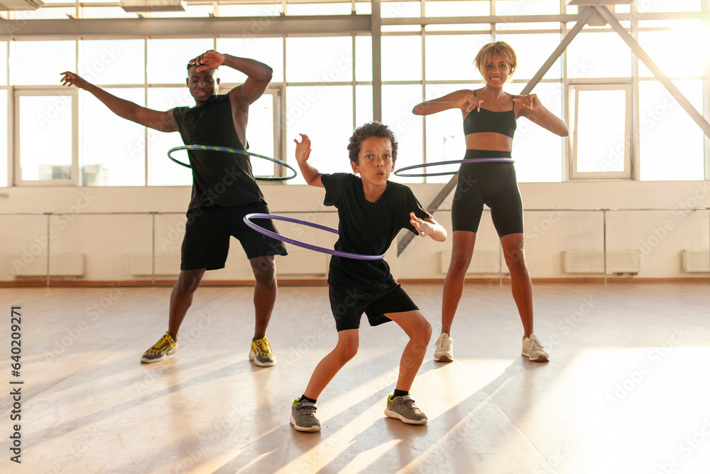 sporty african american family in sports uniform twists hula hoop and does exercises in the gym