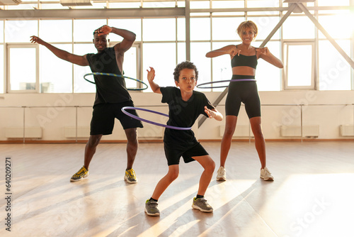 Φωτογραφία sporty african american family in sports uniform twists hula hoop and does exerc