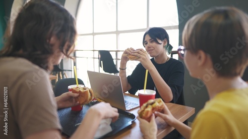group of students sit in a cafe and do a project on a laptop together. business concept of modern lifestyle training and development. students discuss their homework and eat fast food burgers