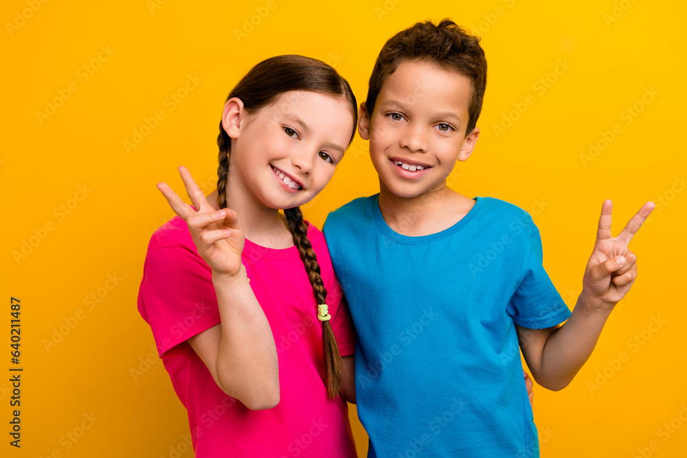 Photo of adorable good mood preteen schoolchildren wear t-shirts showing v-signs isolated yellow color background Photo of adorable good mood preteen schoolchildren wear t-shirts showing v-signs isolated yellow color background