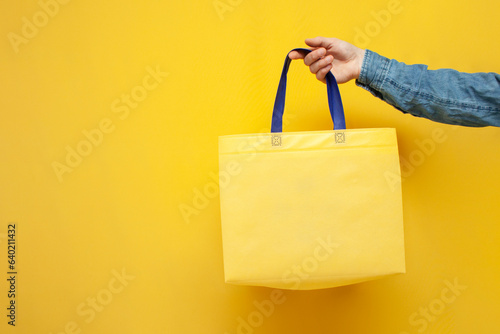 empty fabric eco bag on a yellow background, the guy's hand holds a reusable non-plastic bag