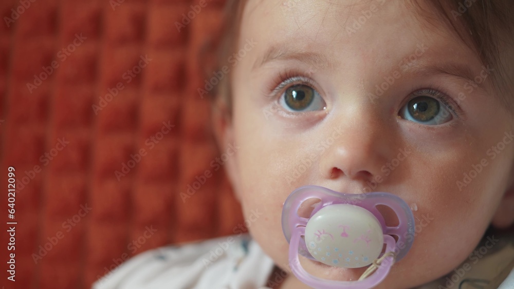 a small newborn sits on the couch with a pacifier in his mouth. happy family childhood dream concept. a little child with a purple pacifier sits and looks at the lifestyle camera close-up a small newborn sits on the couch with a pacifier in his mouth. happy family childhood dream concept. a little child with a purple pacifier sits and looks at the lifestyle camera close-up