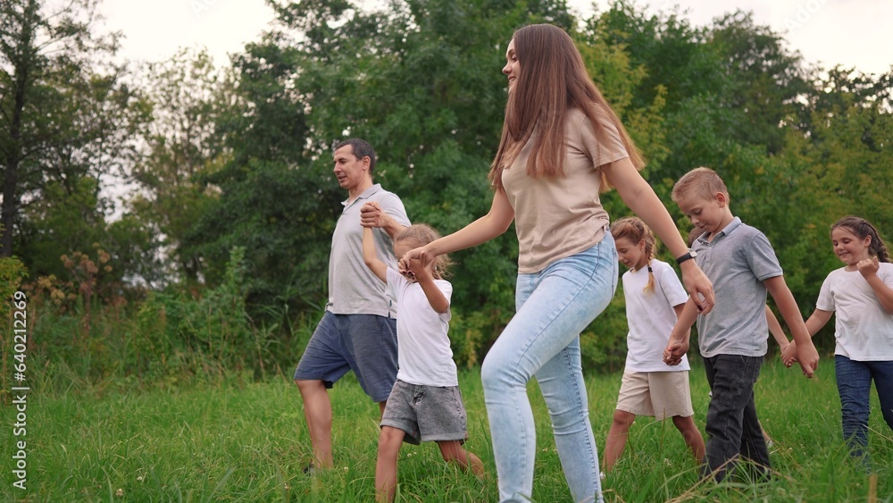 Fototapeta premium family walking on the grass in the park and holding hands. happy family childhood dream concept. a large family walks across the clearing and talks to each lifestyle other. outdoor nature walk