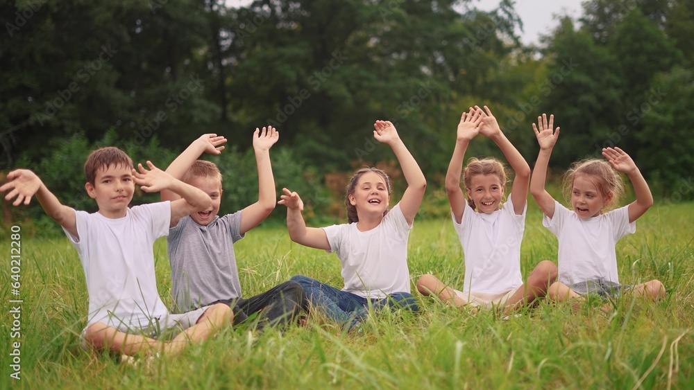 children sit on the grass in the park with their hands up. happy family childhood dream concept. kids are resting in a park in the meadow sitting on the lifestyle grass and stretching their hands up children sit on the grass in the park with their hands up. happy family childhood dream concept. kids are resting in a park in the meadow sitting on the lifestyle grass and stretching their hands up