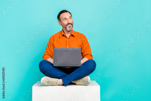 Full length photo of dreamy charming man dressed orange shirt texting modern gadget looking empty space isolated turquoise color background