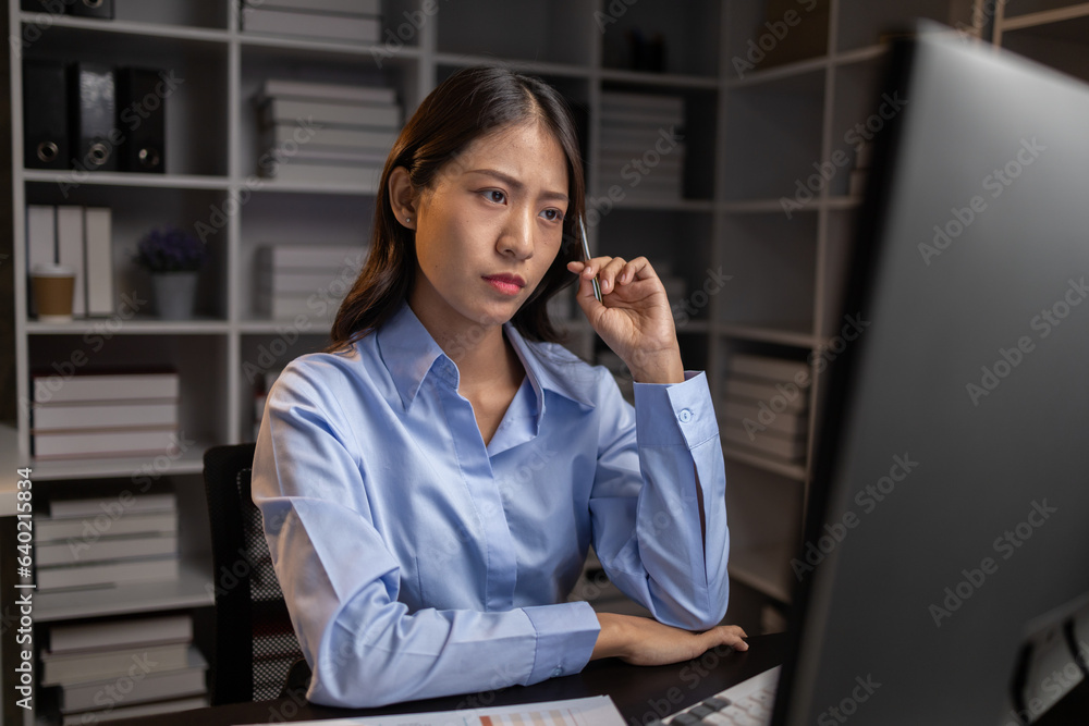 Asian woman sitting in the office working overtime in the middle of the night, employee working overtime to get work done on time. The concept of overtime and hard work of company employees. Asian woman sitting in the office working overtime in the middle of the night, employee working overtime to get work done on time. The concept of overtime and hard work of company employees.
