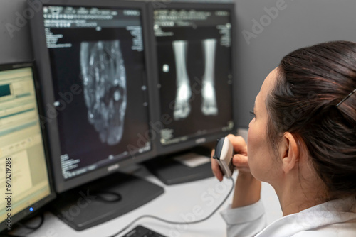 Fotografering radiology doctor examines foot, ankle x-ray, mr image and reports with microphone looking computer screen, X-ray analysis room reading X-rays of a heel, toe and other parts of the body