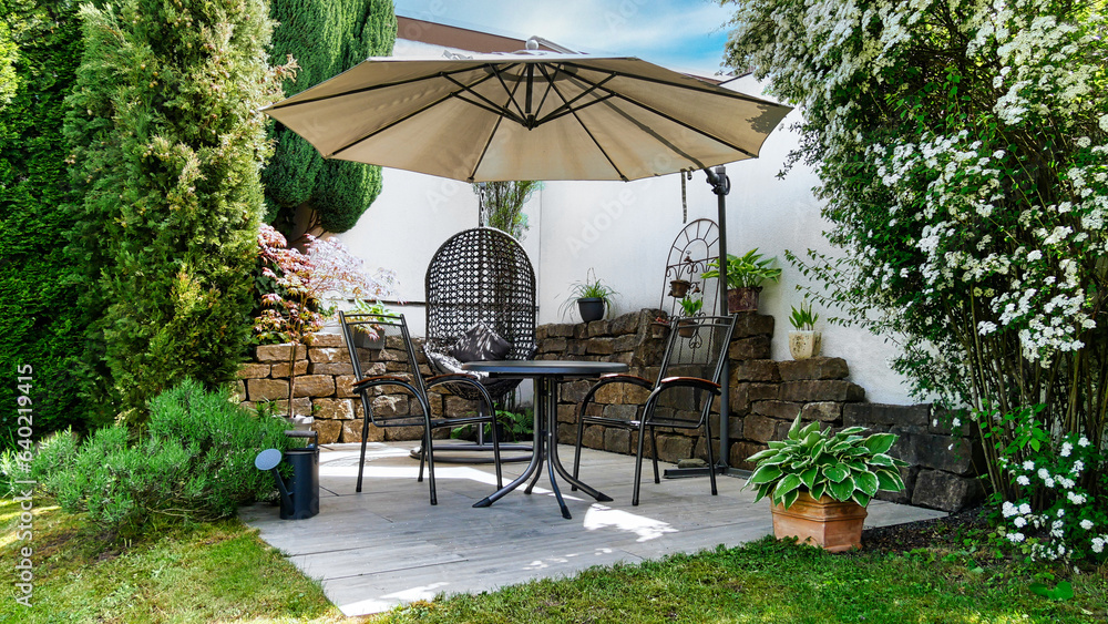 Obraz premium Gartenterrasse mit Hängesessel, Sonnenschirm und Sitzmöbel in einer Gartenecke mit Säulen-Faulbaum und umgeben von Pflanzen und Zypressen 
