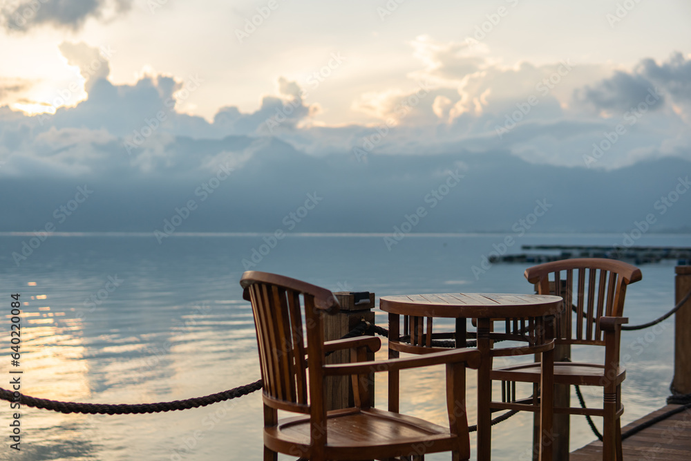 Sunset view in Maninjau Lake with chair and cafe table for relaxing. Beautiful landscape in West Sumatra, Indonesia. Evening sun, clouds, and mountains.