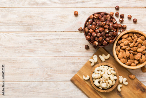 Assortment of nuts in wooden bowl on colored table. Cashew, hazelnuts, walnuts, almonds. Mix of nuts Top view with copy space