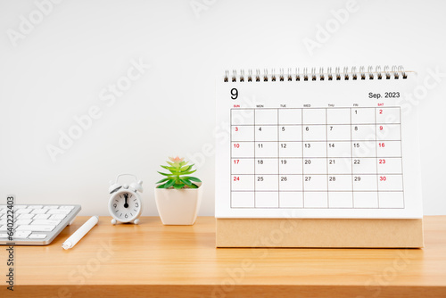 The September 2023, Monthly desk calendar for 2023 year on wooden table with alarm clock.