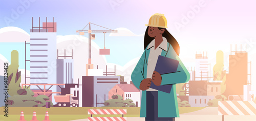woman architect or engineer in uniform standing near unfinished building construction site background