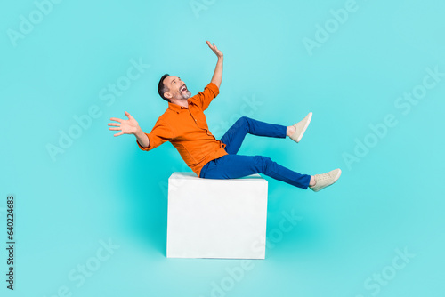 Portrait of careless playful man dressed orange shirt falling from platform look empty space isolated on turquoise color background