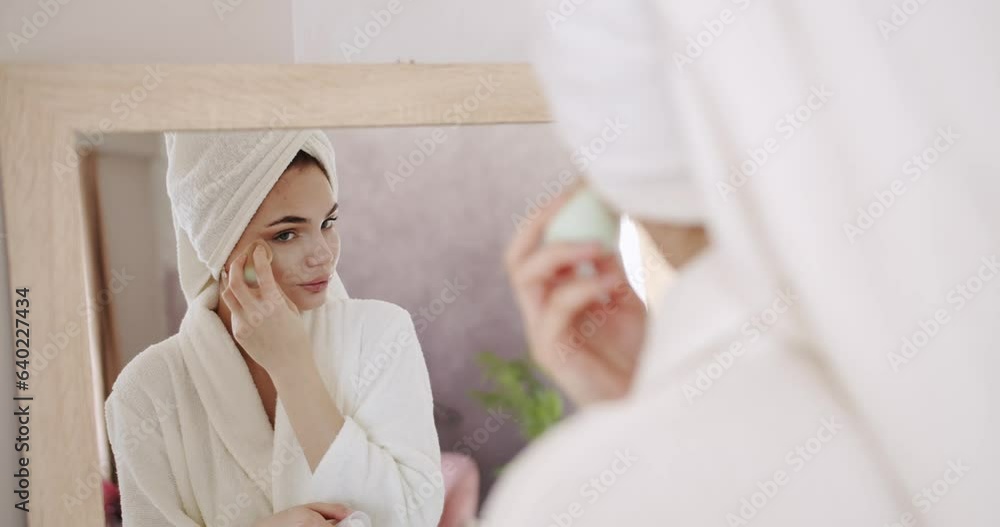 Slow motion of woman with beautiful face and perfect skin just cleaned from impurities pampering. Young female wearing towel on head and bathrobe looking in mirror at home. morning skincare routine. Slow motion of woman with beautiful face and perfect skin just cleaned from impurities pampering. Young female wearing towel on head and bathrobe looking in mirror at home. morning skincare routine.